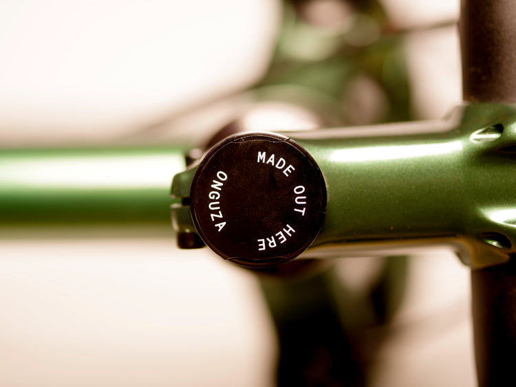 A detailed image of the signature brand line "ONGUZA Made Out Here" top cap, a magnetic headset top cover, in black, etched in white with a lazer. It is on a Boomslang Green hardtail Rooster mountain bike.  